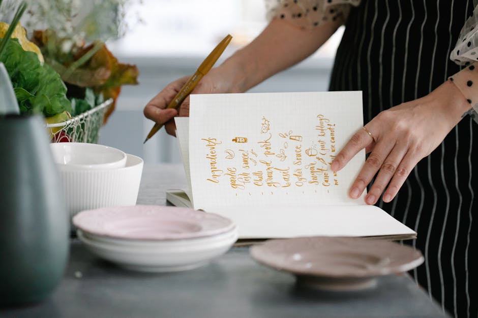 Woman writing a recipe in a notebook in a kitchen setting, surrounded by kitchenware.