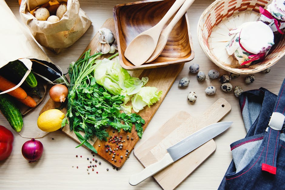 Top view of fresh vegetables, herbs, and kitchenware on a wooden table ready for cooking.