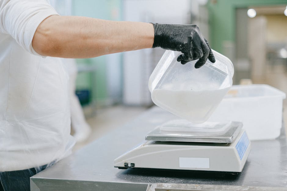 Chef in a kitchen carefully measuring ingredients using a digital scale.