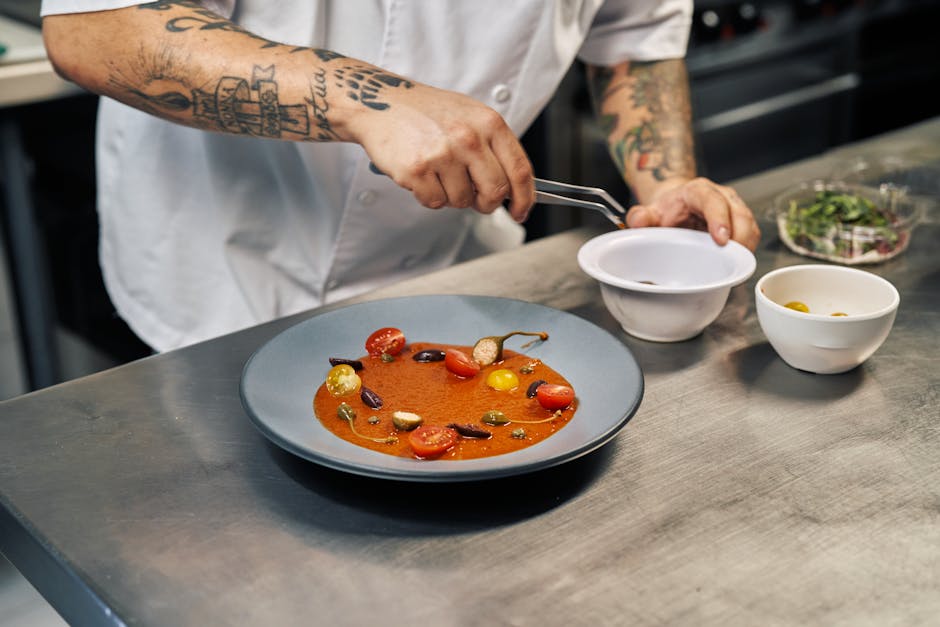 Chef expertly garnishing a tomato soup with cherry tomatoes and herbs in a professional kitchen.