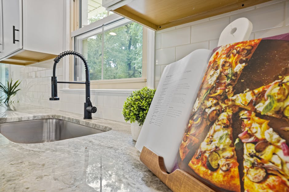 Stylish kitchen featuring a marble countertop, modern sink, and an open cookbook with a pizza recipe.