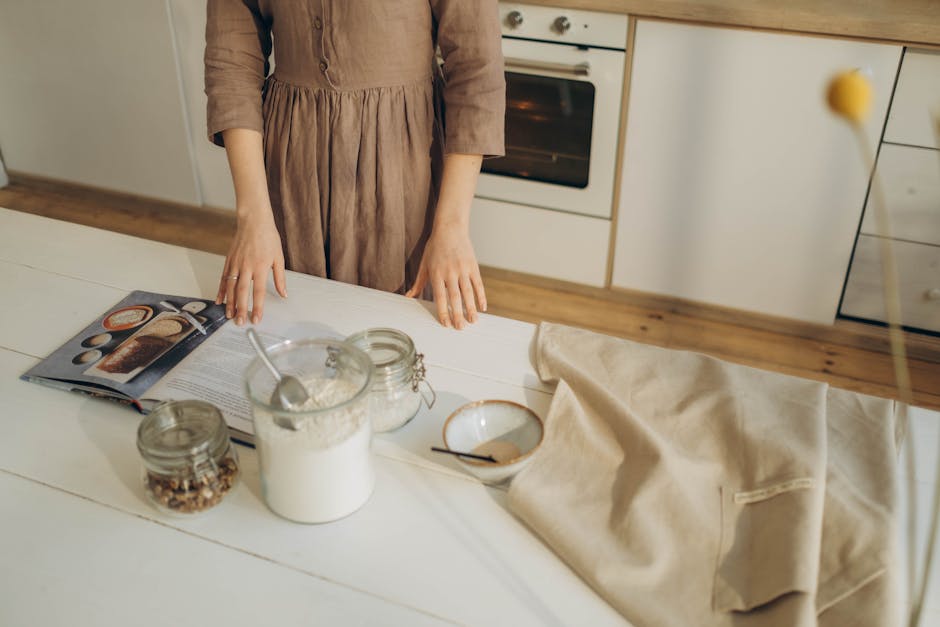 A person prepares ingredients on a wooden kitchen table with a cookbook for baking.